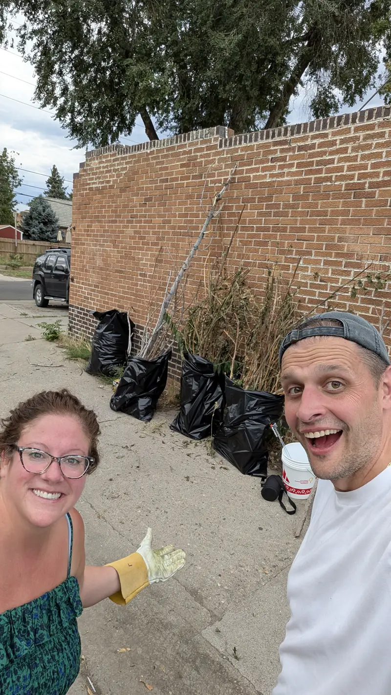 Two volunteers grinning next to a row of full trash bags